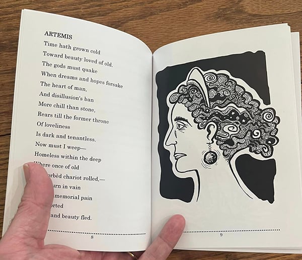 A hand holds open the book showing pages 8 and 9, showing text on the left and Artemis on the right.
