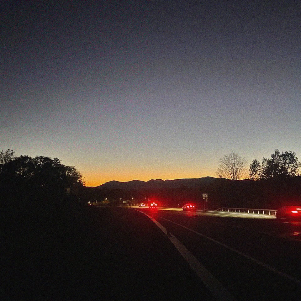 brake lights illuminate on a downhill slope overlooking the Catskills at sunset