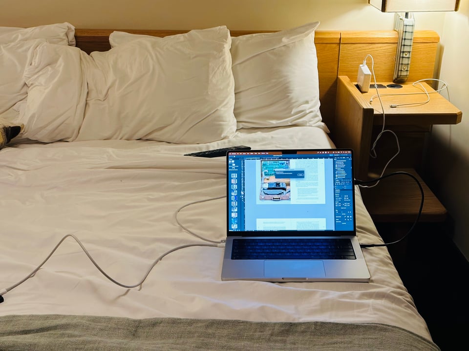 A computer on a hotel bed, with InDesign assembling the book for the last time