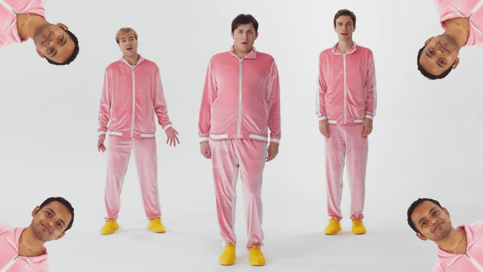 The four members of Boy Throb standing singing in their signature attire, pink tracksuits with yellow sneakers. From left to right: Anthony, Evan, and Zach, with Darshan peeking out of every corner.
