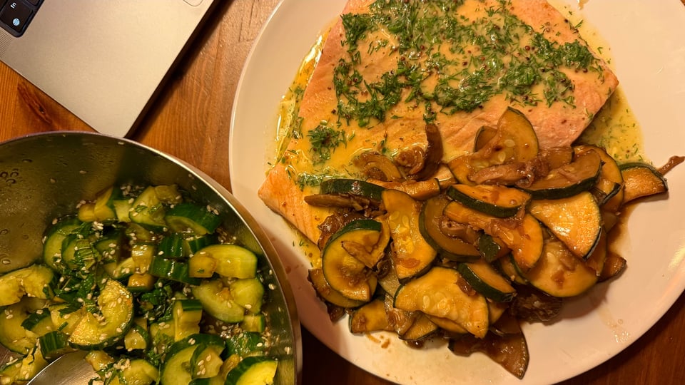 A plate with salmon and courgette, a bowl with cucumber and a piece of laptop.