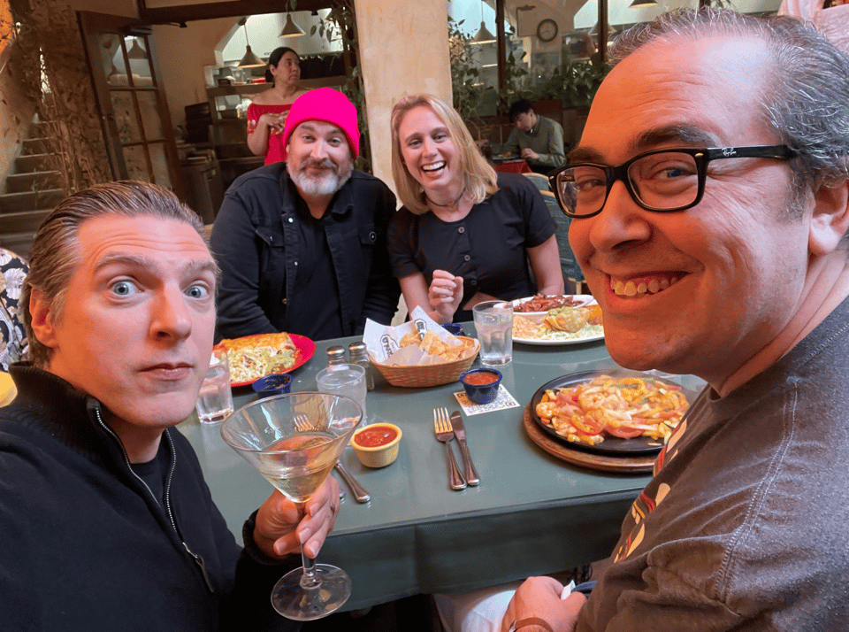 Four people at a Mexican restaurant smiling at the camera, food on the table