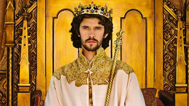 Actor Ben Whishaw, a young white man with dark hair and beard, wearing a crown and holding a sceptre. There is a lot of gold in the throne behind him.