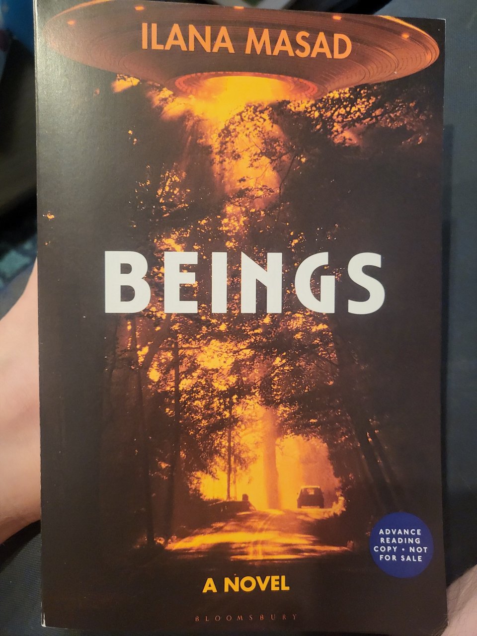 Photo of the galley of BEINGS, which features an orange tinted photograph of a car driving down a wooded road and a UFO high above shedding light on the scene