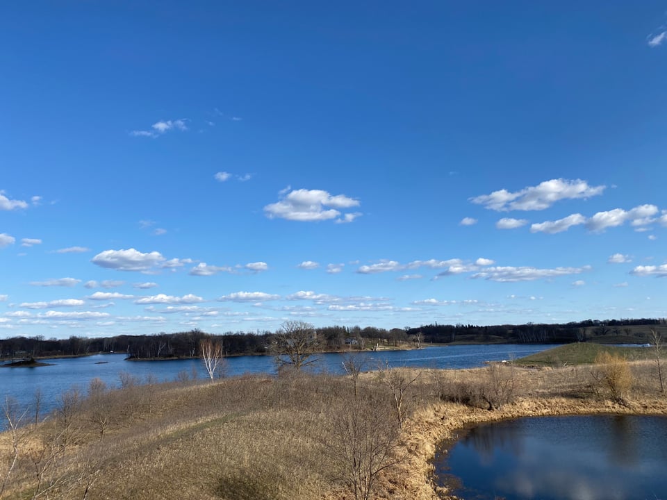 a landscape image of sky, blue lake, and brown land mass in West Central Minnesota, white clouds dot the sky