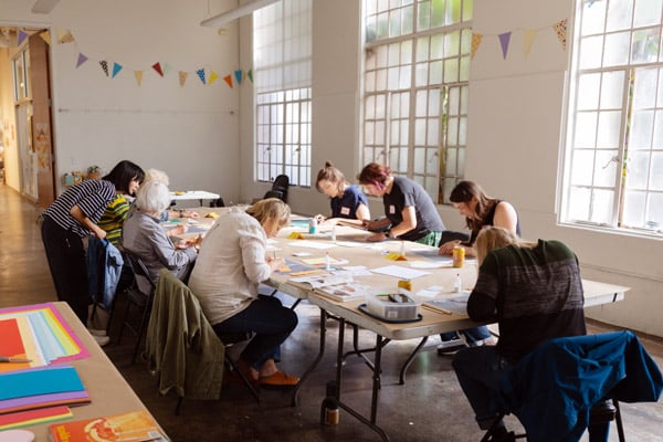 Group of students working at a large communal table in a room with large windows