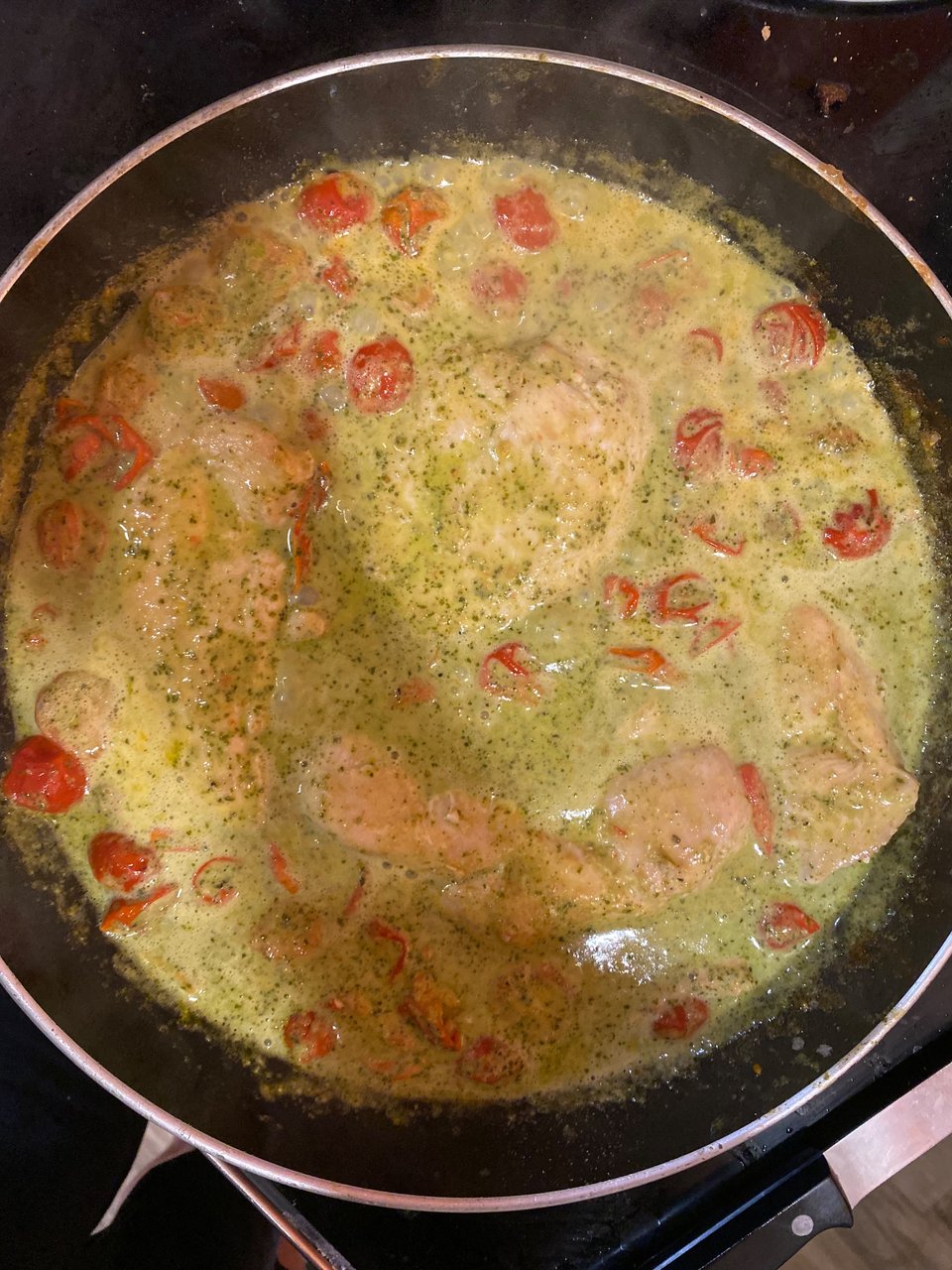 The creamy tomato pesto chicken in the pan on the stove.