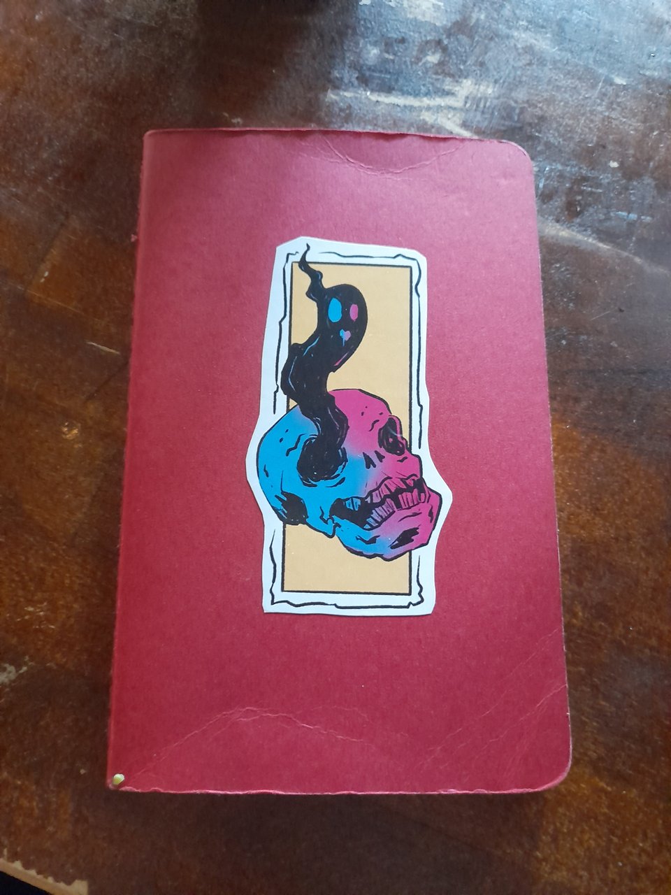 A photo of a small notebook. It has a sticker on it showing a ghost floating out of a skull.