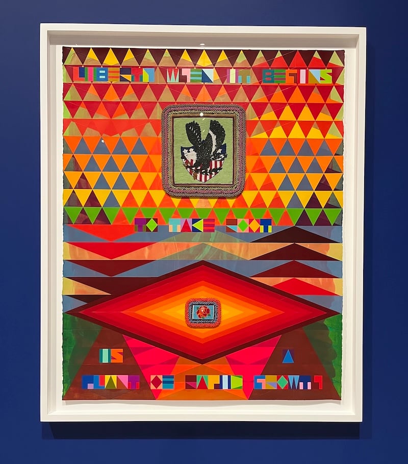 Framed abstract work on paper featuring a pattern of multicolored triangles across the top, extending down to the middle of the image. Superimposed on these is a beaded image of a bald eagle flying across a shield with white stars on a blue ground and red stripes. Below, a pattern of larger triangles takes over, topped by a large diamond that is yellow in the center and radiates out in shades of orange and red to its brown border. At the center is another beadwork depicting a red rose. Blocky, multicolored lettering interspersed from top to bottom reads liberty when it begins to take root is a plant of rapid growth. 
