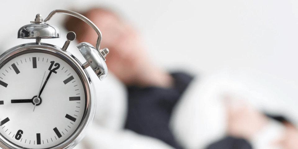 A person asleep with an alarm clock in the foreground.