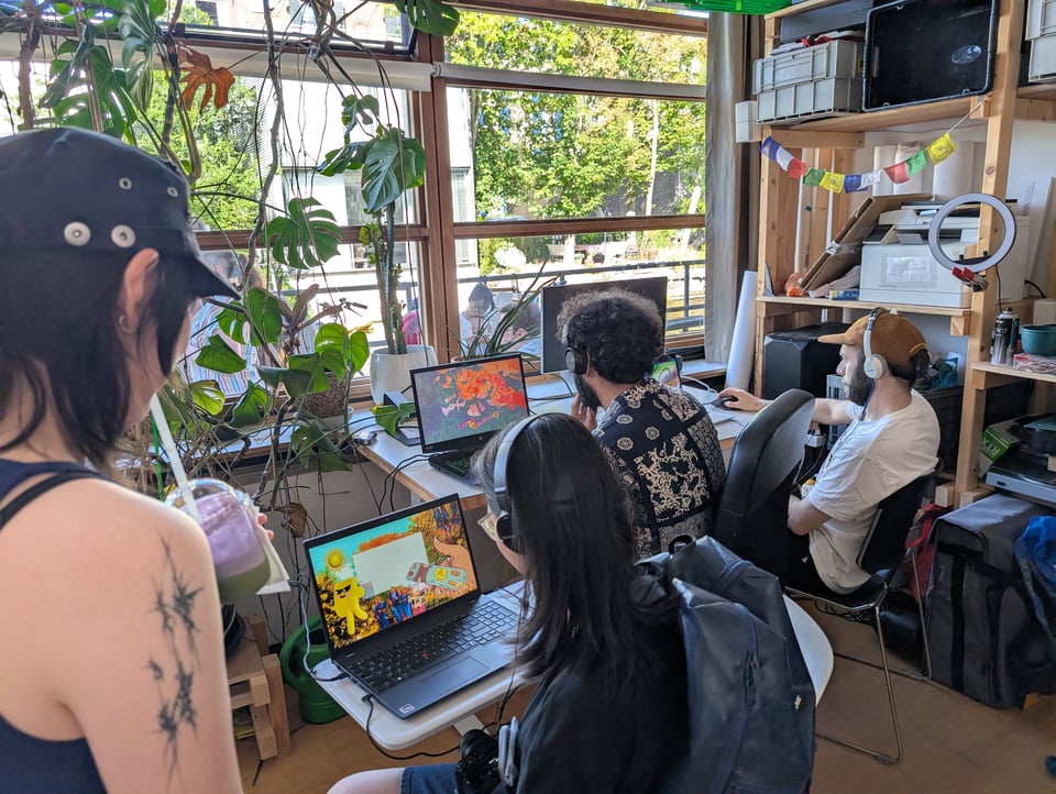3 people play a colourful game on laptops arranged around a window. A fourth watches on, standing.