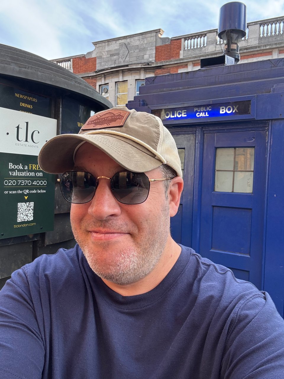 neil standing in front of a blue phone booth in london - a tardis, if you will