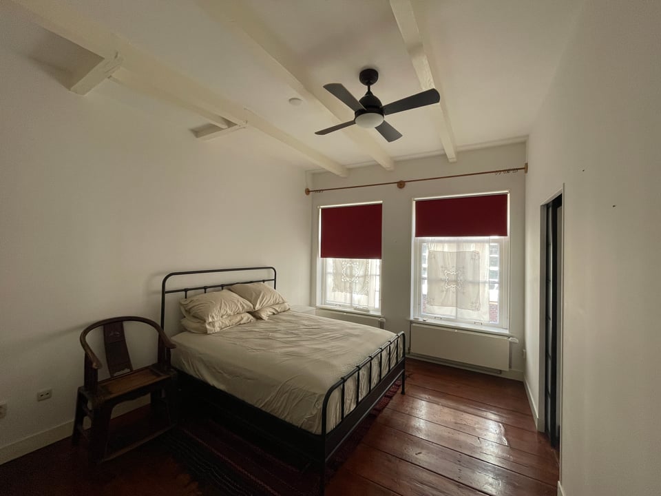 A bedroom with a double bed made up and an old wooden chair next to it.