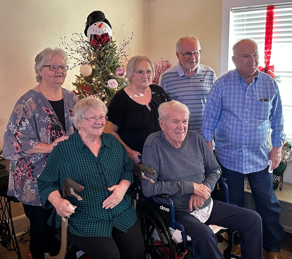 Photo of 6 older folks — 3 men and 3 women — in front of a Christmas tree