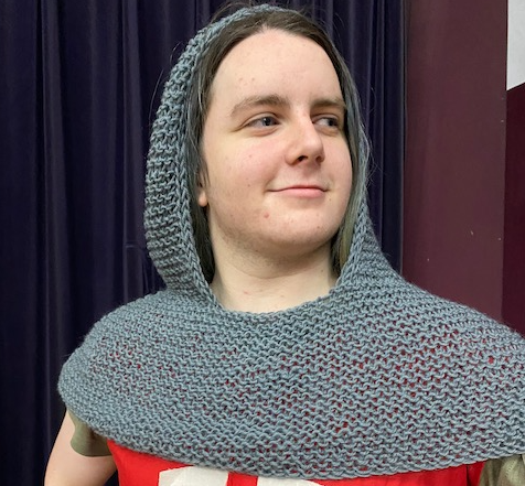 a person wearing a knitted chain mail coif, what looks like metal covering head and shoulders, but is actually yarn