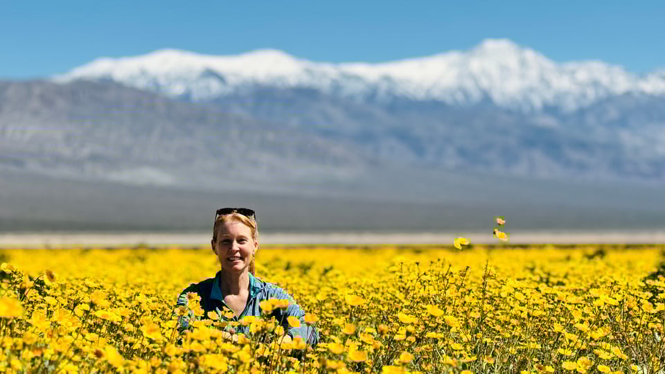 Julie sitting in a field of wildflowers with snowy mountains in the background