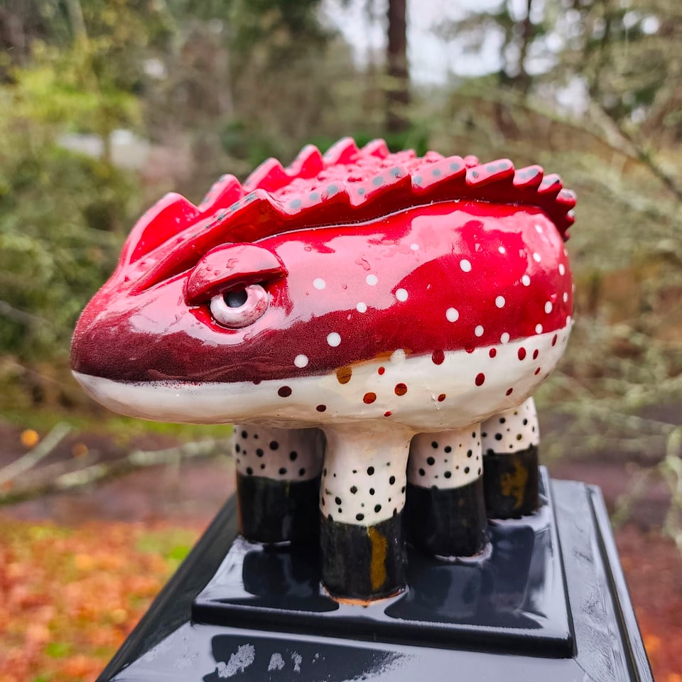 A sculpture of a grumpy, ceramic creature. Its body is oval-shape with two ridges along its back. It's red and white, with dots where the colors meet, and its six legs are tipped in black.