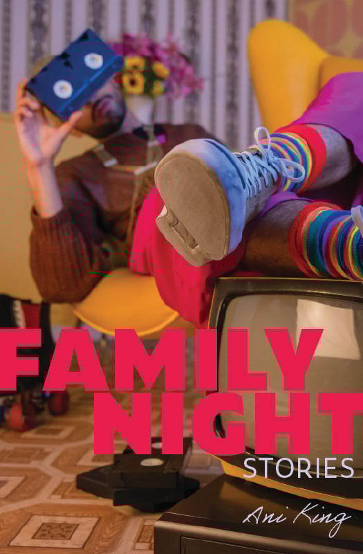 Picture of the Family Night book cover, which features a person in bright clothes and rainbow socks reclining in a yellow retro chair, with their feet propped up on an old CRT television. The person is holding a VHS tape up over their face, and a pile of VHS tapes sits on the floor. The title is in bright pink, all capital letter.