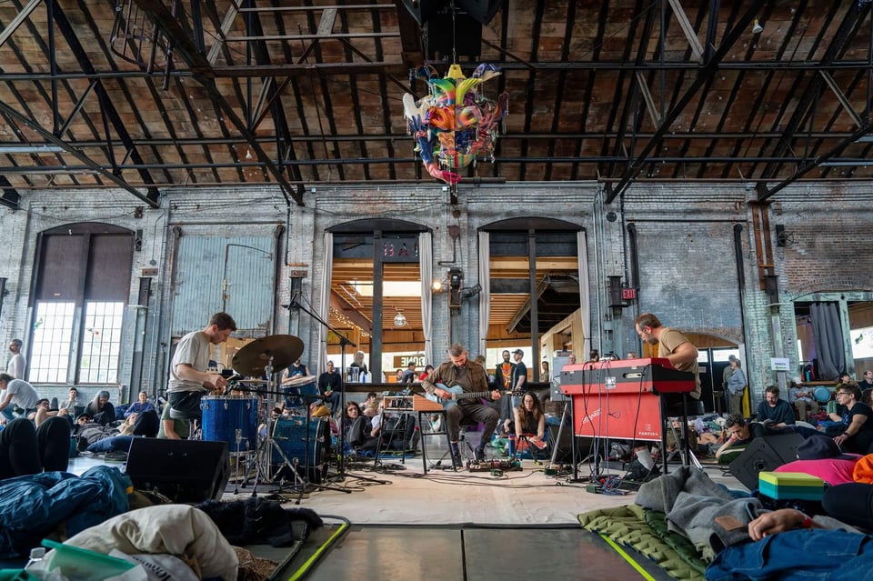 A Gracelee sculpture hovering over a band playing to a crowd in sleeping bags.