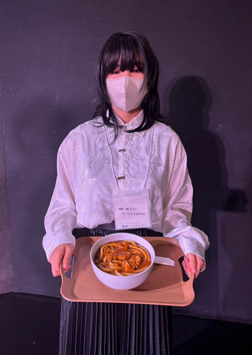 A person wearing a white shirt holds a tray with a bowl of curry udon