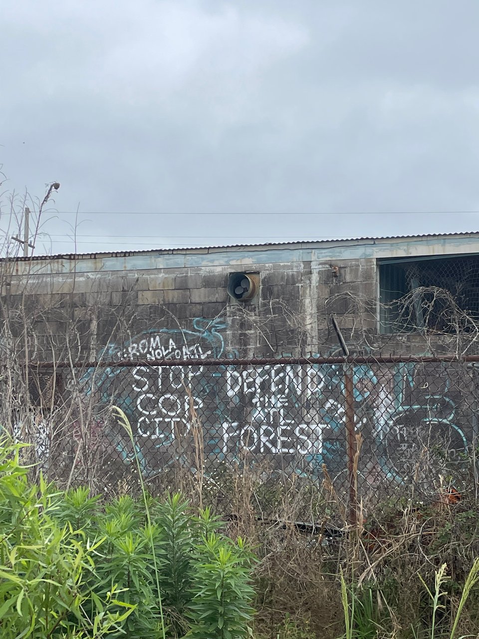 graffiti on a building behind a chainlink fence that read "From NOLA to ATL, STOP COP CITY, DEFEND THE ATL FOREST"