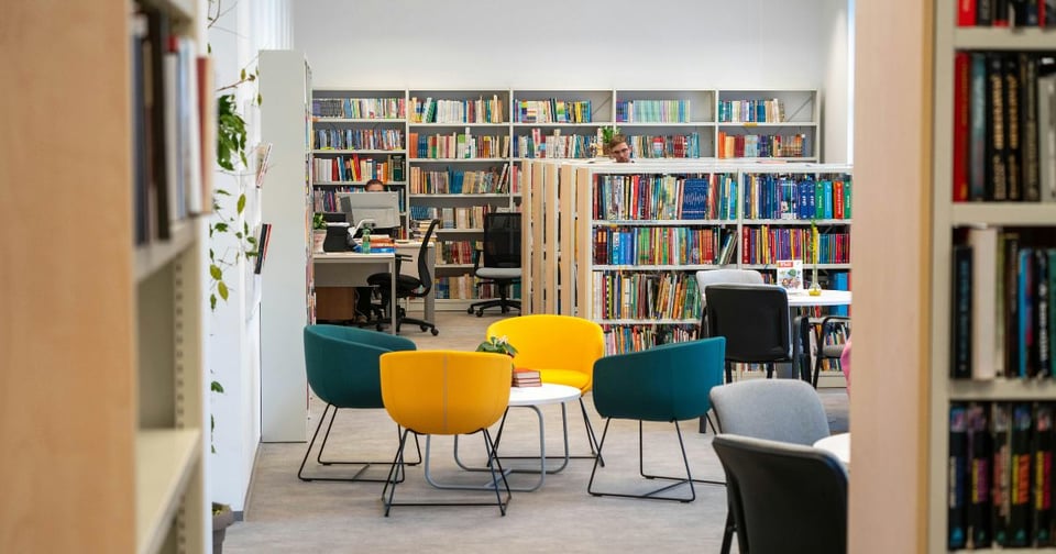 Stock image of the inside of a school library. It has colorful chairs and shelves of books.