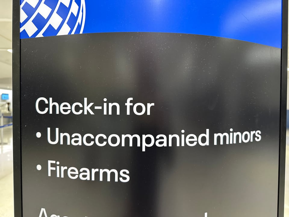 photo of United Airline sign in Newark reading "Check-in for Unaccompanied minors, Firearms."