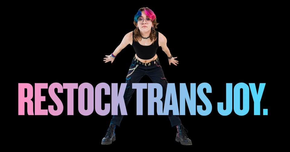 Image of a person behind a sign that says restock trans joy