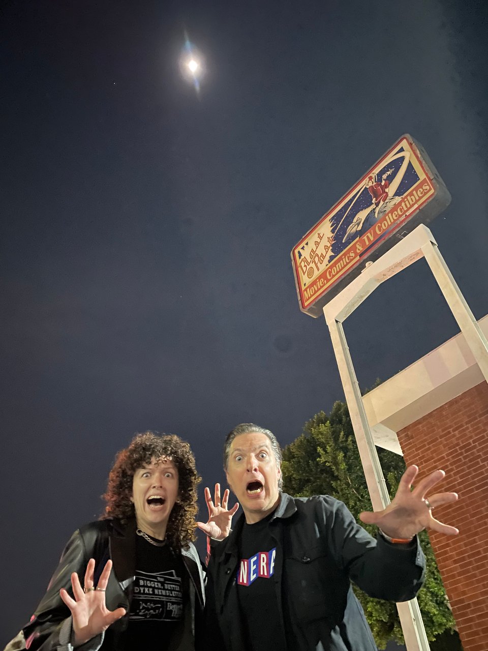 A woman and a man scream at the camera in mock terror. Behind them is a sign for the collectible shop Blast From the Past. The moon glows