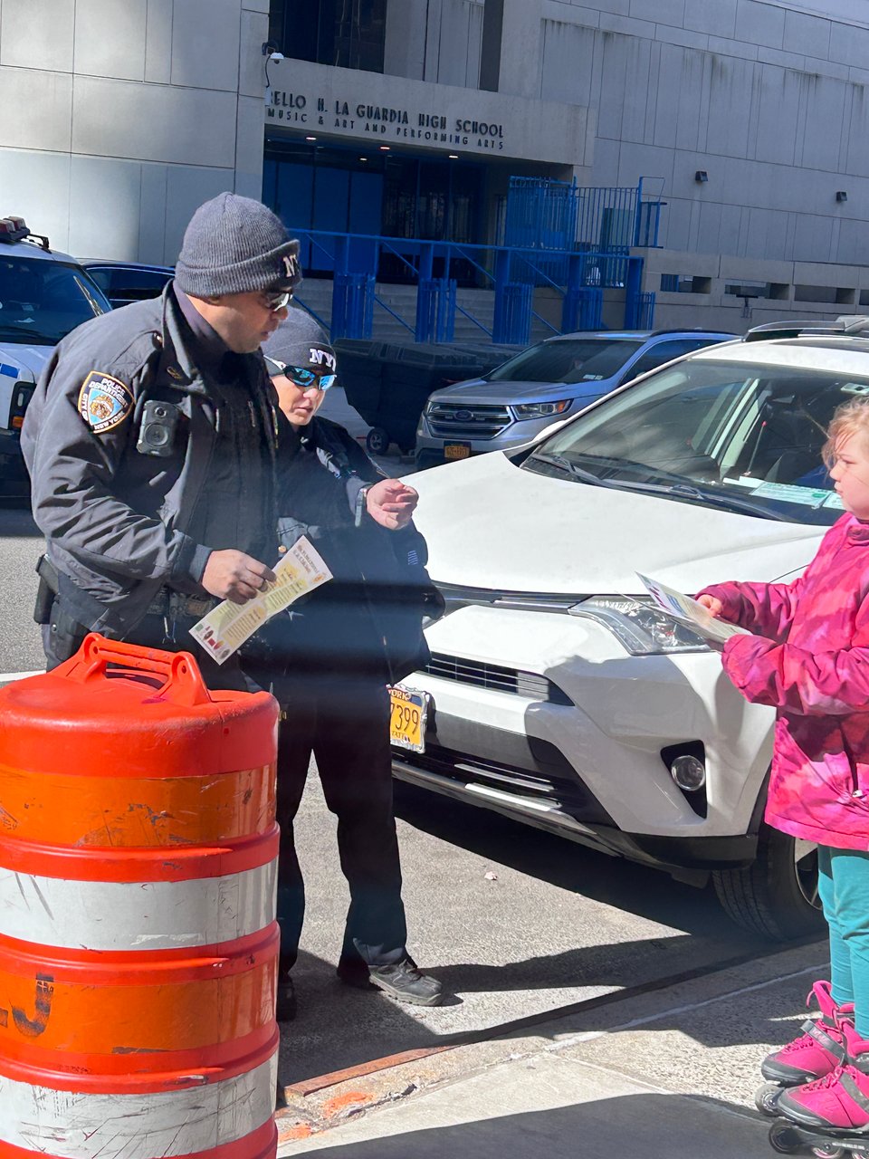 A little girl in a pink jacket and pink skates hands a flyer about why AI is bad to an NYPD cop