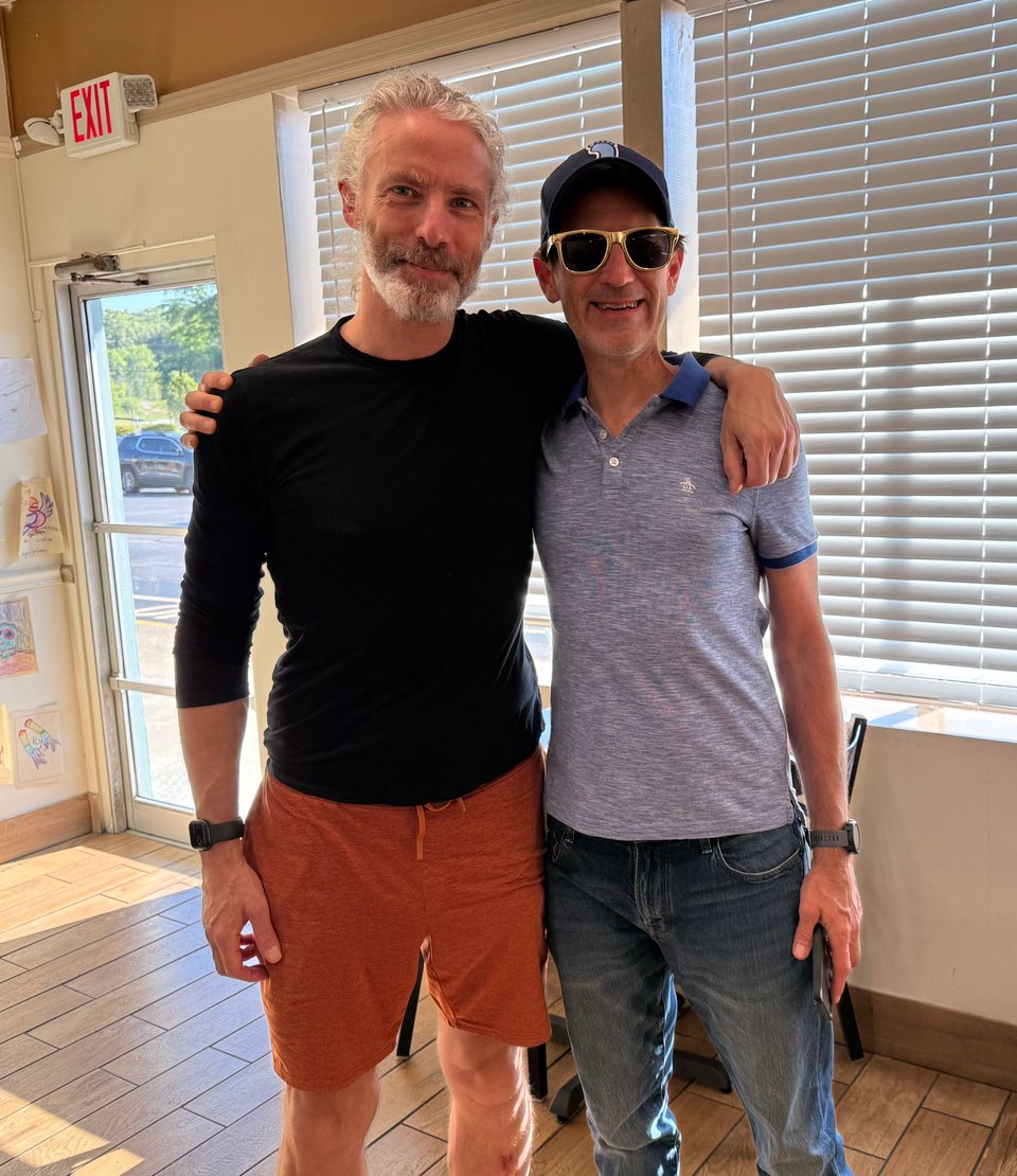 photo of 2 men in their 50s with arms over shoulders and smiling for the camera. They look pretty good for their age