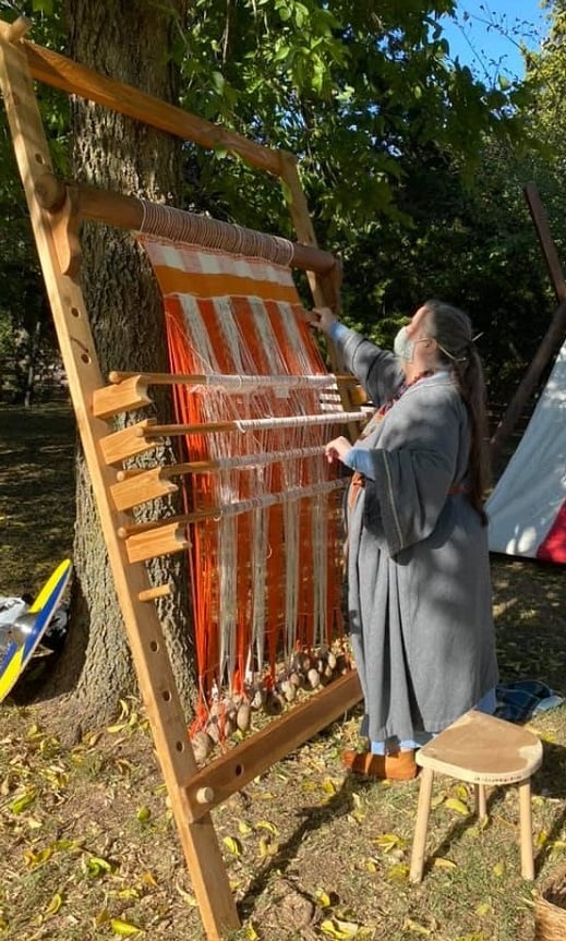 Woman working upright loom outdoors