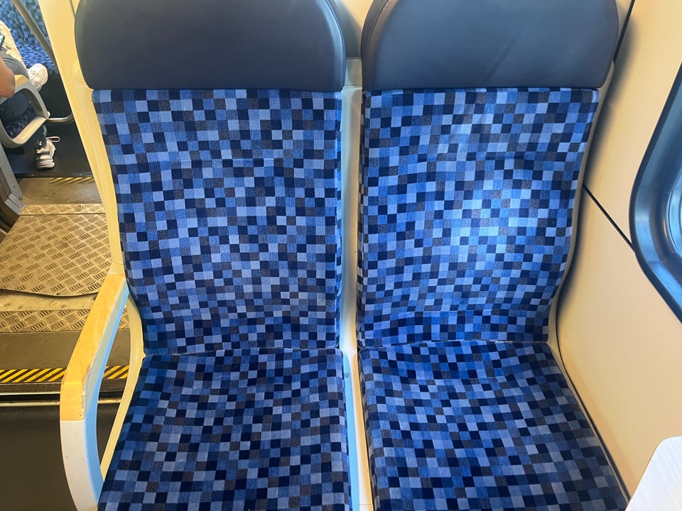 A pair of train seats whose covers are a series of small squares in varying shades of blue.