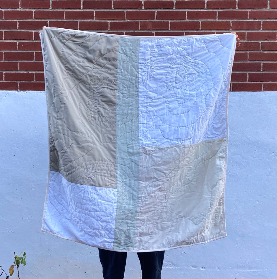 Quilt made with different patches of white and beige fabric squares, and a freehand organic design sewn on top