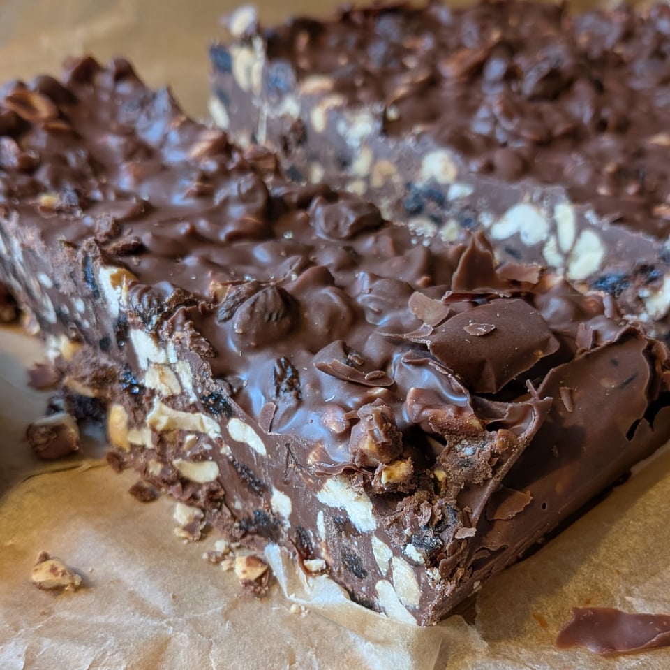 A close up of a slice of a chocolate bar, exposing how it is full of peanuts and cashews and raisins.