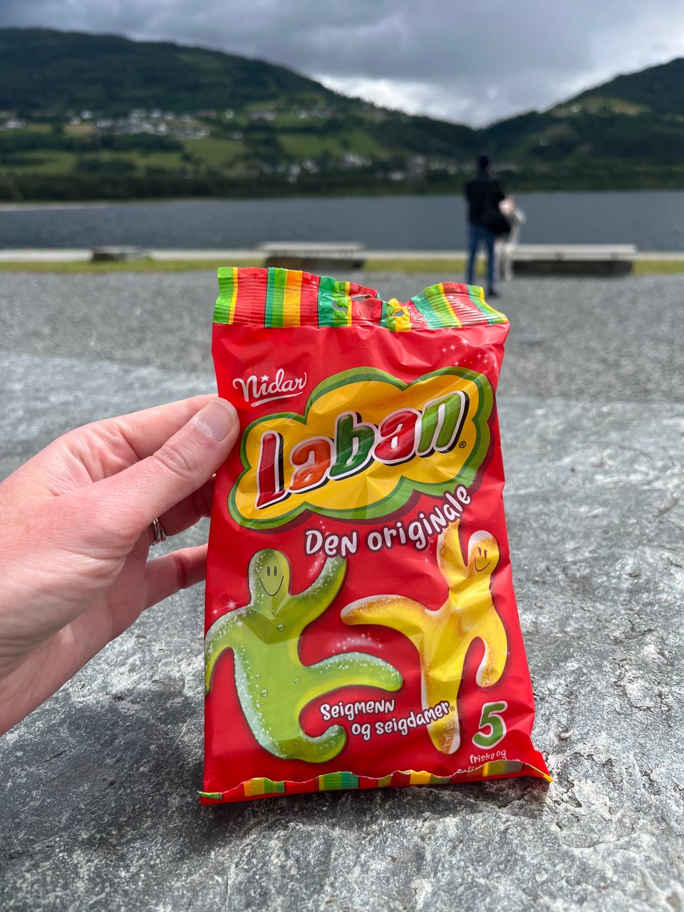 Hand holding bag of gummy candies in front of water and mountains