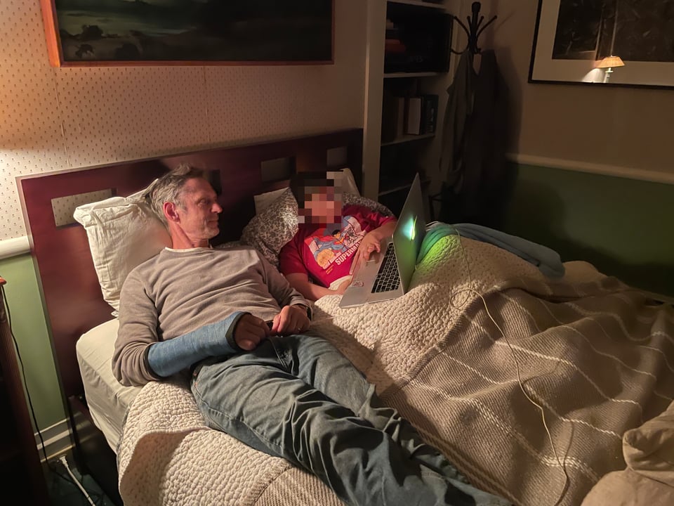Two people rest on a bed watching a movie on a laptop.