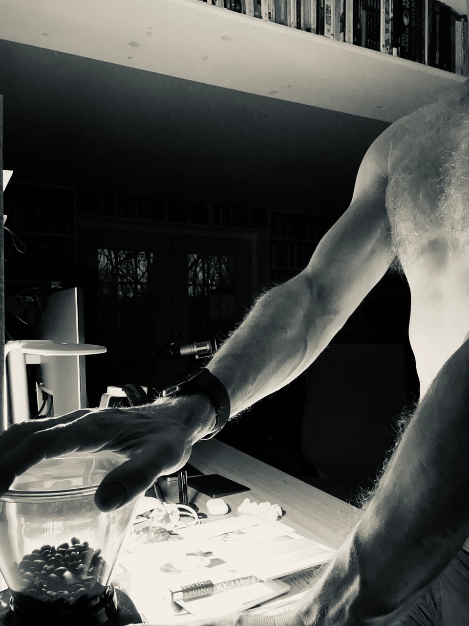 b/w photo of shirtless man grinding coffee beans in a Baratza Encore grinder. You can see his arms and some of his chest, but not his face