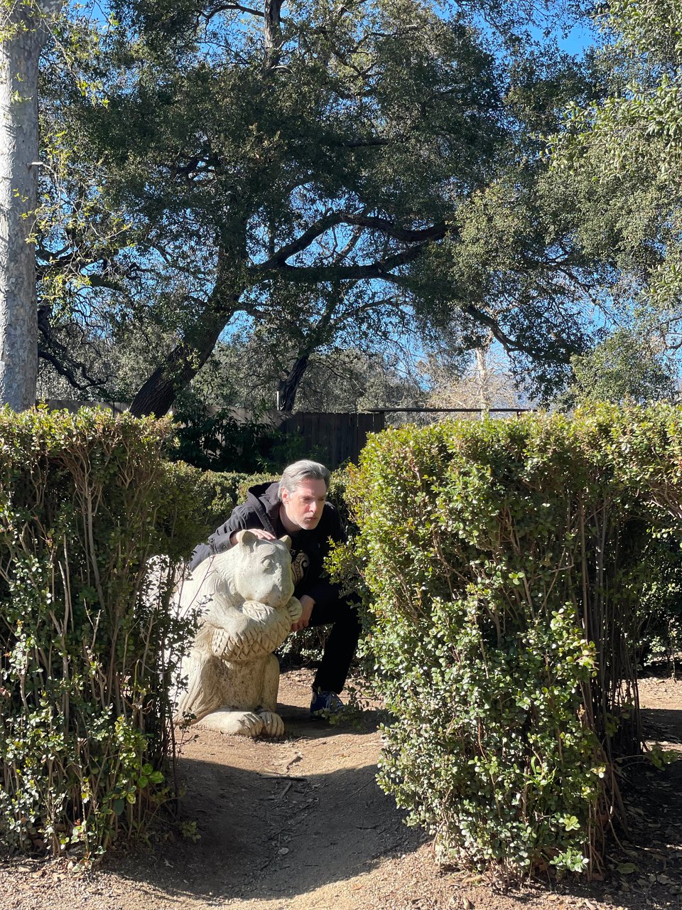 A man hunches down by a thoughtful squirrel statue in a garden