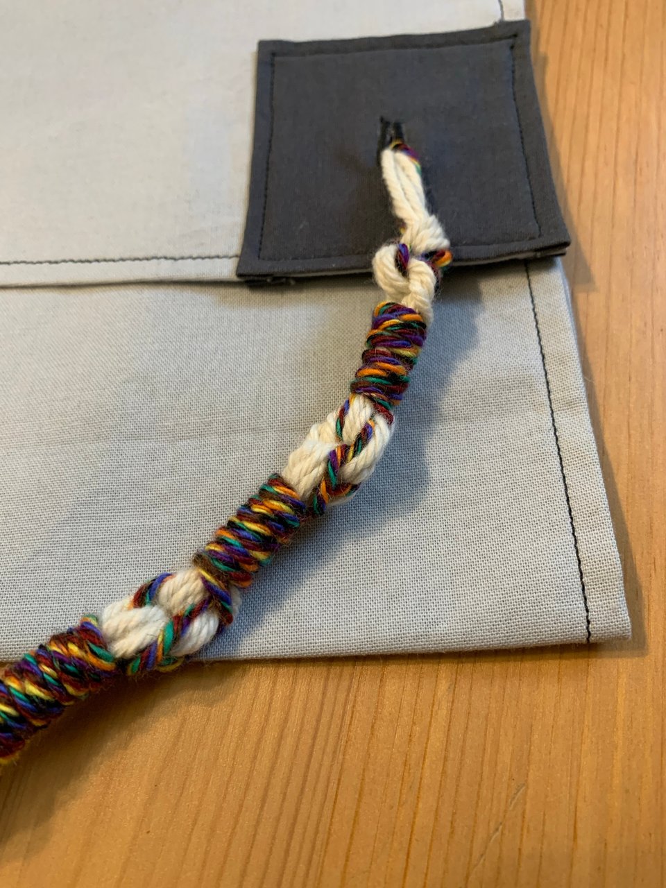 a large rainbow and white sample tzitzit tied onto a corner. this close-up shows the rainbow threads wrapping around the white.