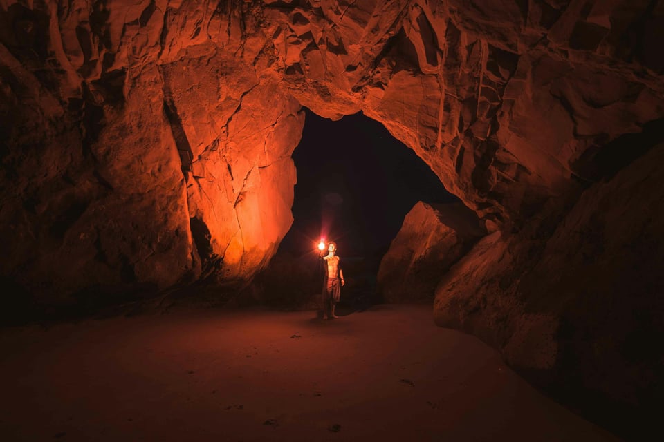 Person standing and holding a lamp inside a cave.