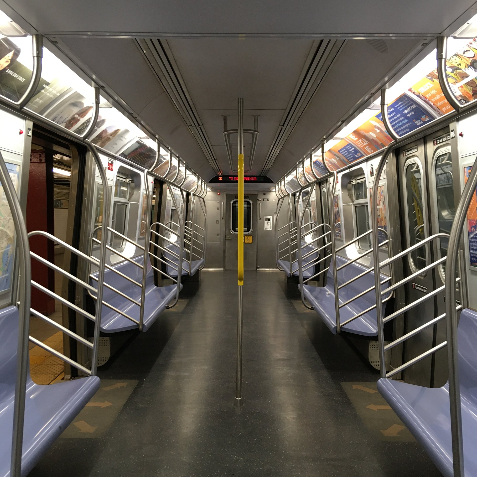 A photo of an empty NYC Metro car, lined with blue seats, silver metal poles, and advertisements above the seats.