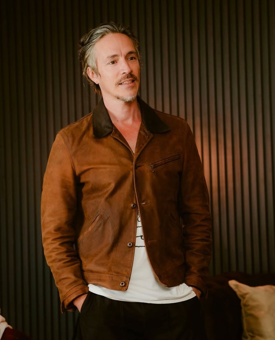Photo of musician/artist Brandon Boyd, in a brown jacket with a white T-shirt underneath
