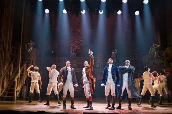 A still image from the stage musical Hamilton (2015). The ending pose for the musical number "My Shot", with John Laurens, Alexander Hamilton, Marquis de Lafayette, and Hercules Mulligan posting under the lights while the backup dances face away from them.