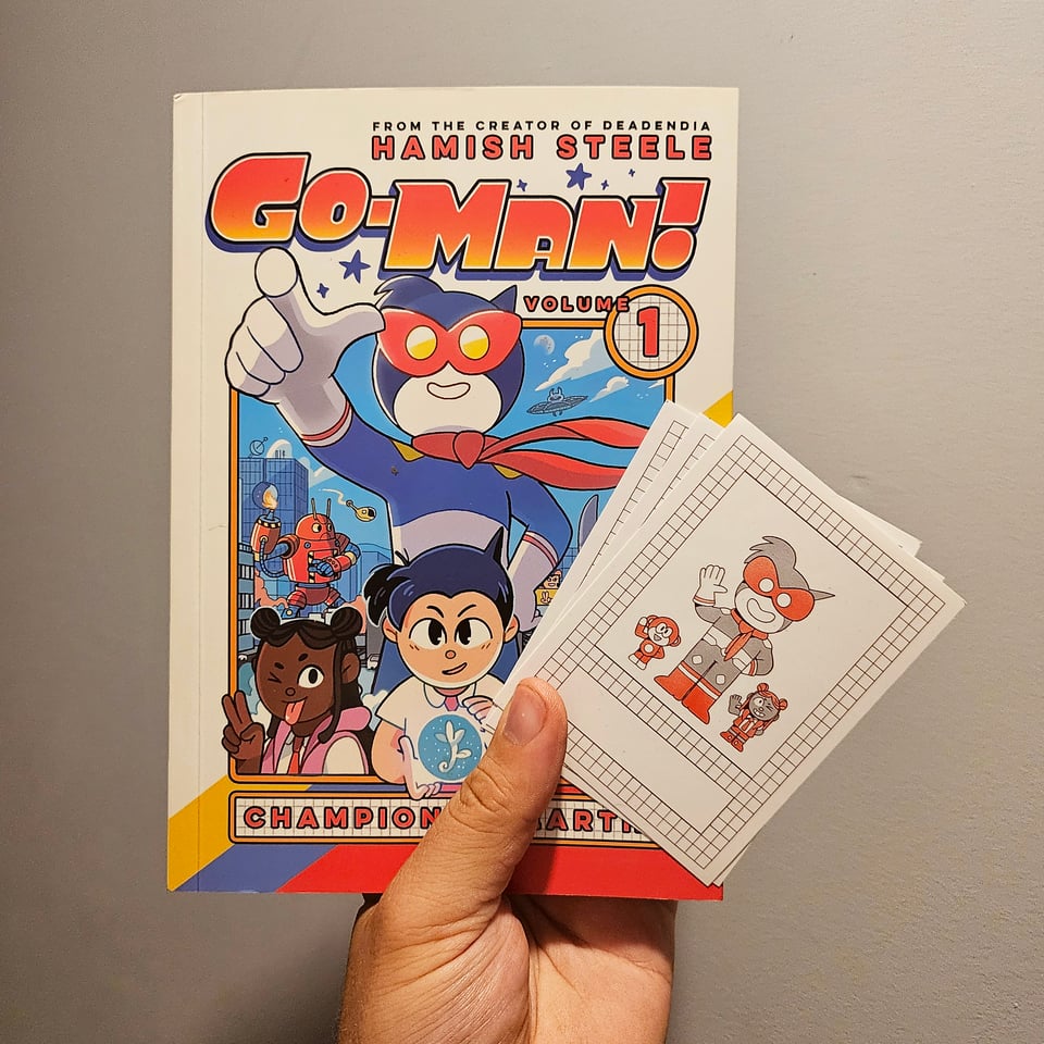 A hand holding up a copy of the book Go-Man Champion of Earth as well as a little bookplate featuring characters from it.