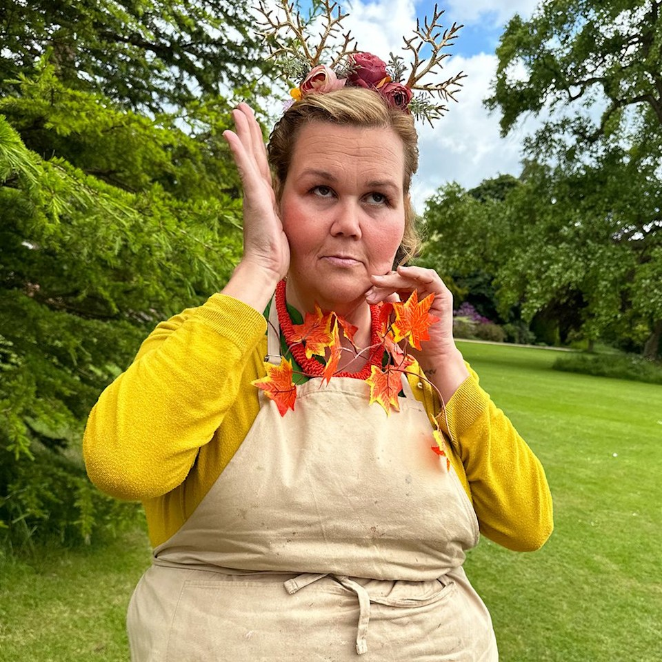 A person holding fall leaves to her face and making a goofy expression