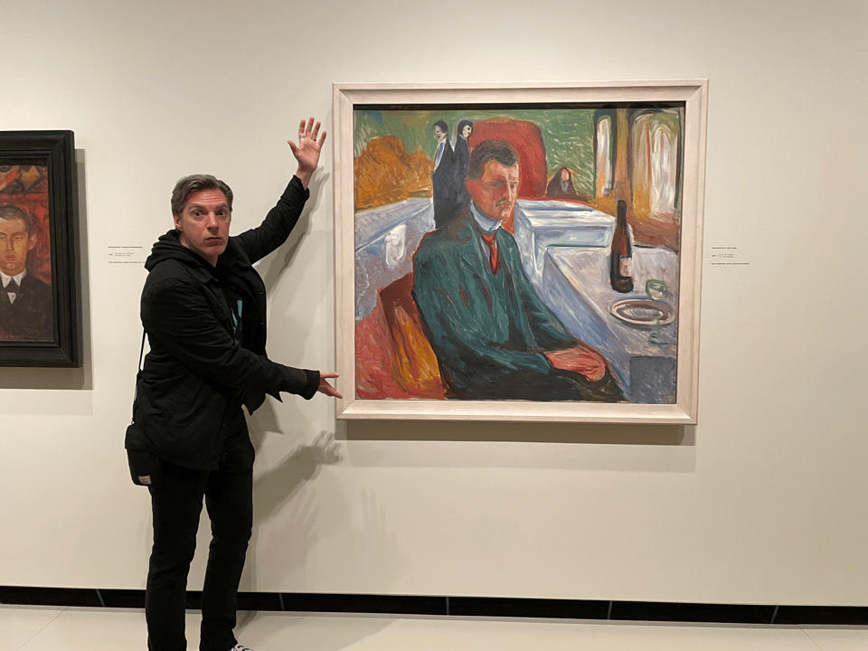 A man gesticulates at an Edward Munch self-portrait of himself looking pensive with a bottle of wine and an empty glass
