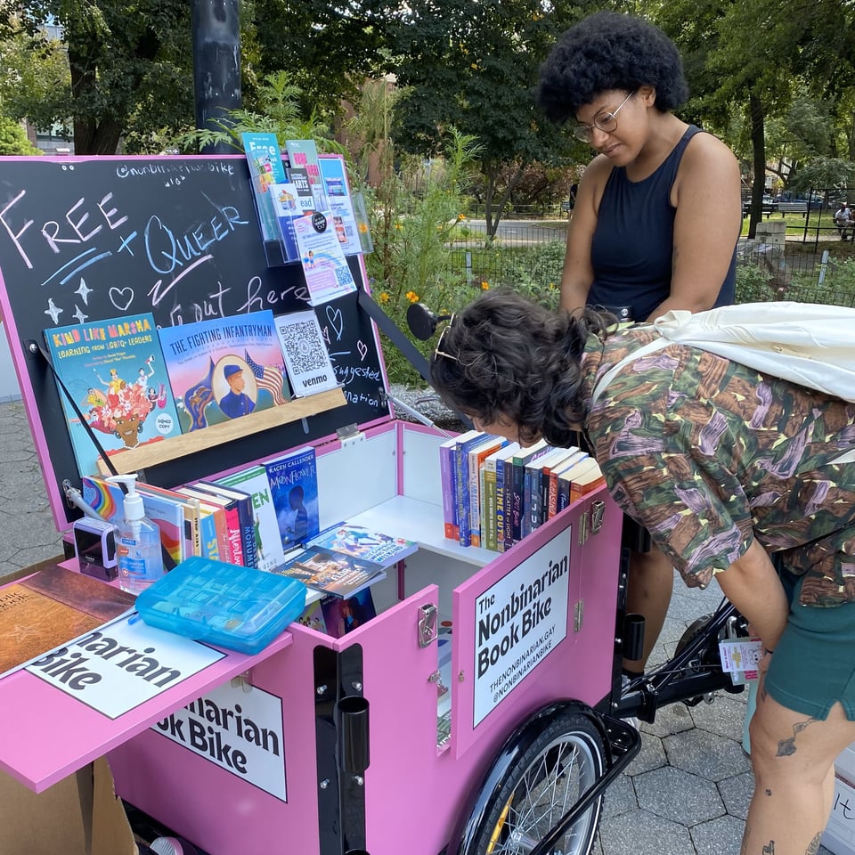 Two people admire the offerings on display at the Nonbinarian Book Bike Book Drive