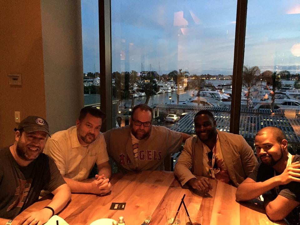 five handsome guys at a restaurant table with a window in the background, low lighting