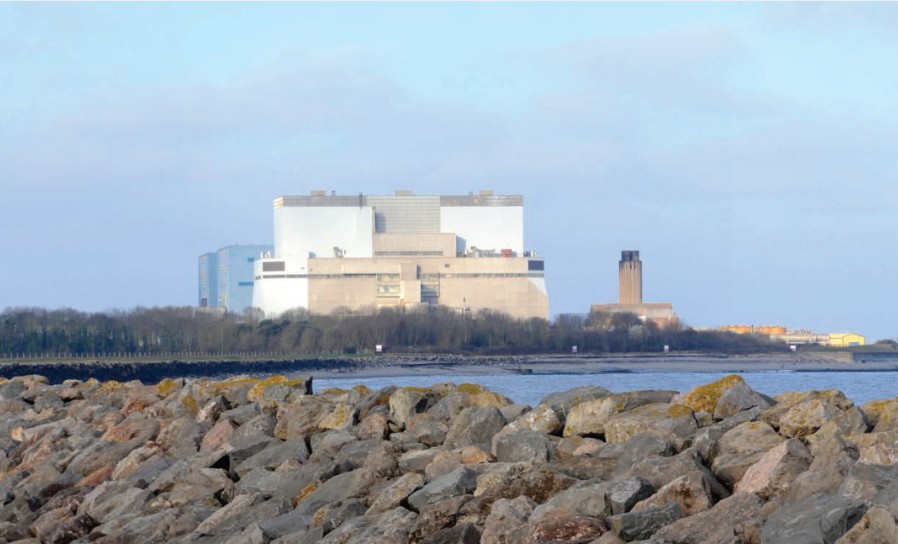 A huge concrete power station sitting on the edge of an estuary. It's hard to get a sense of scale, but the mature trees in front of it barely reach a quarter of its height. Behind it, almost disappearing into the blue-grey sky, are two smaller blocks.